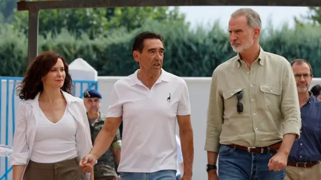 Isabel Diaz Ayuso walks alongside Marian Nunez and King Felipe. Felipe wears a green shirt and jeans