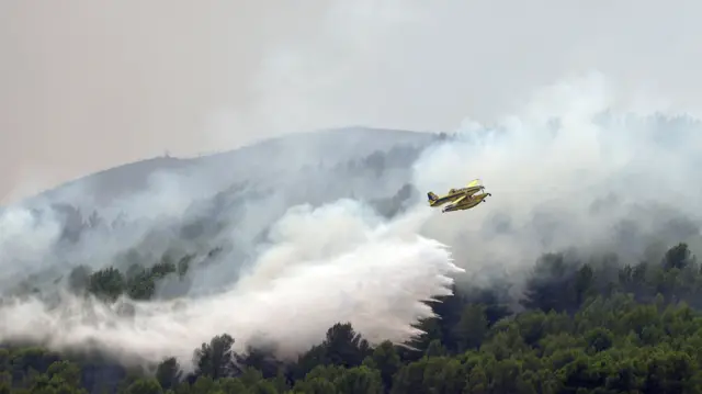 A small yellow plane drops water over a smoky forest