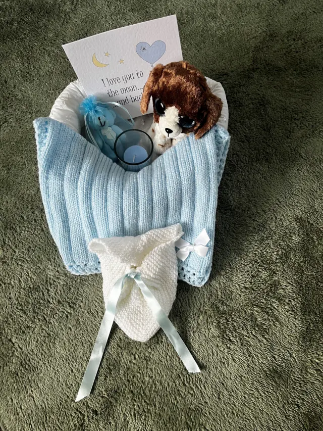 A memory box with a teddy a tiny knitted hat and blanket and a card which reads 'I love you to the moon and back'