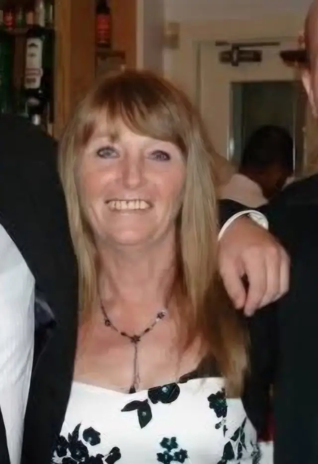 A woman with long light brown hair is wearing a black and white floral dress and is smiling at the camera.