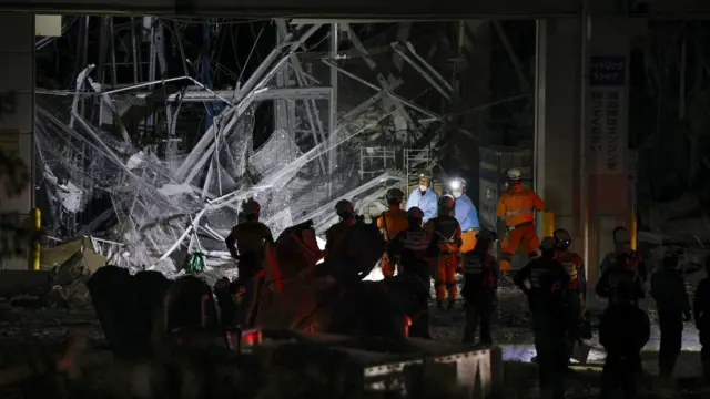Workers are visible in the dark in orange overalls as they search a mangled structure