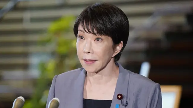 Japanese Prime Minister Sanae Takaichi in a grey blazer at a podium