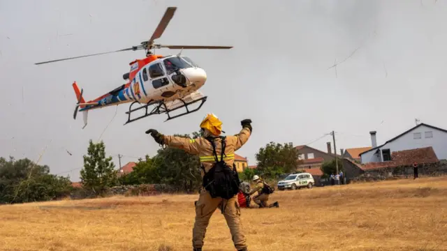 A firefighter in uniform waves his arms as a helicopter lands in a field.
