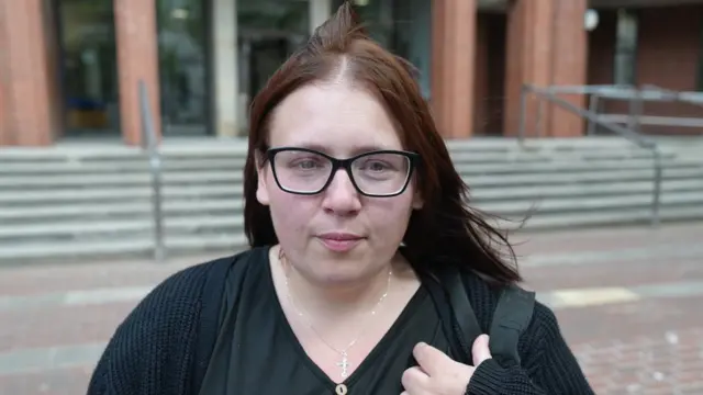 Jasmine Beverley standing outside Hull Crown Court she has long brown hair and is wearing glasses and a black top with silver necklace