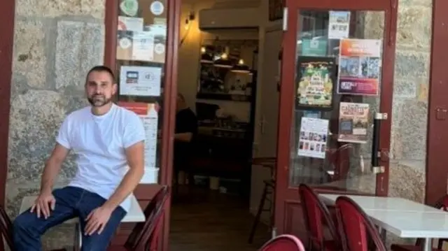 Fabien pictured wearing jeans and a white t-shirt in front of his establishment