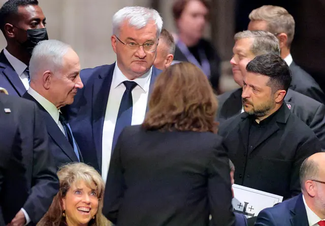 Nenyahu in dark suit faces Zelensky in dark suit, surrounded by people