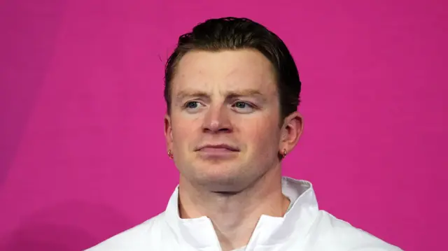 Adam Ramsay-Peaty looks at the camera in front of a pink background following his swim at the Commonwealth Games