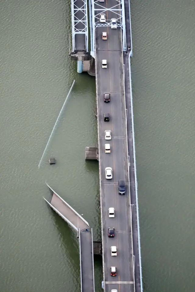 A bridge is collapsed as cars travel alongside it
