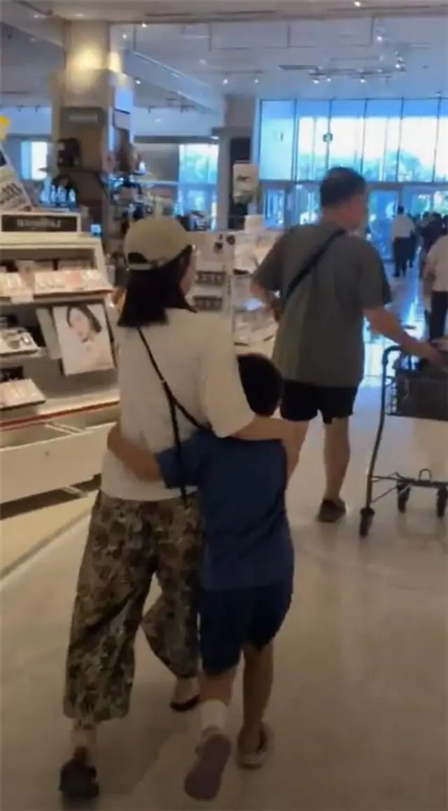 A screenshot from the video, a woman has her arm around a child as they walk out of the building