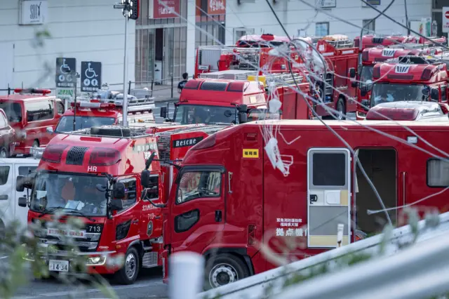A group of red emergency vehicles are clustered on a road.