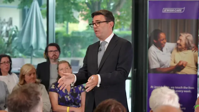 Andy Burnham, who has short dark hair and glasses, speaks while wearing a business suit