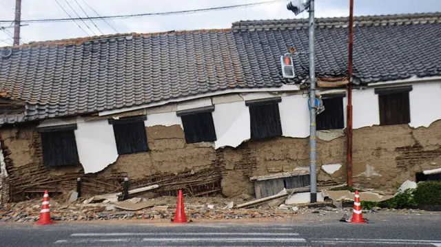 A collapsed traditional building with grey-tiled roof by a road