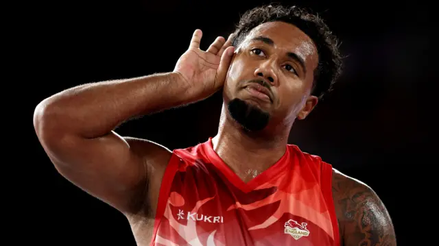 Dwayne Lautier-Ogunleye, wearing England's red basketball vest, cups his hand to his ear to celebrate the semi-final victory over New Zealand