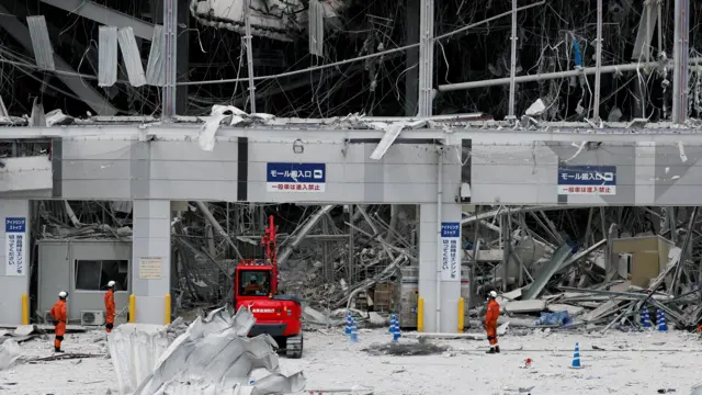 Workers sift through rubble of a destroyed entrance to the Aeon Mall
