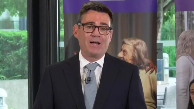 Andy Burnham, who has short dark hair and glasses, speaks while wearing a business suit