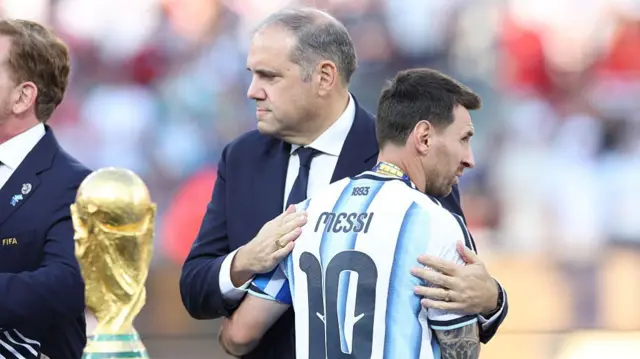 Lionel Messi of Argentina looks dejected as he is embraced by Victor Montagliani, president of CONCACAF, while walking past the FIFA World Cup trophy after the FIFA World Cup 2026 Final match between Spain and Argentina at New York New Jersey Stadium on July 19, 2026 in East Rutherford, New Jersey. (