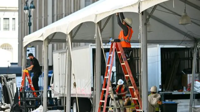 People in high-vis on ladders put up white gazebos