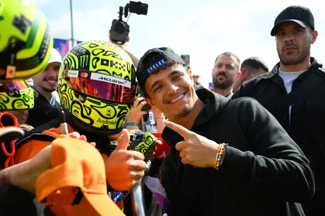 Lando Norris poses with a fan dresses in full race suit and helmet