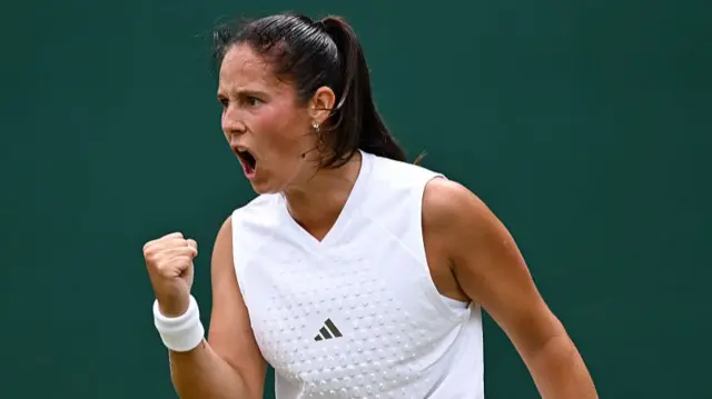 Daria Kasatkina, wearing a sleeveless white top, raises a clenched right fist and shouts