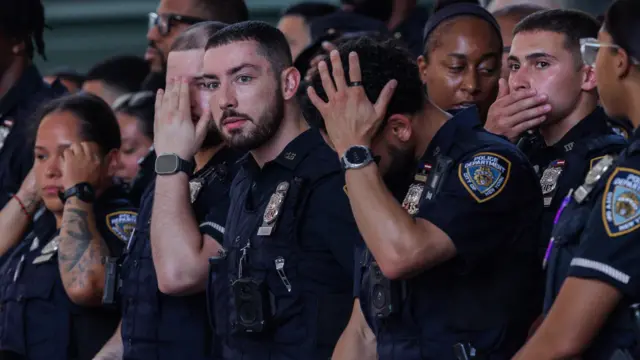 NYPD officers wipe their heads as they stand in formation. A close up photo.