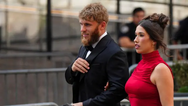 A man with a long beard wearing a tux and a woman in a red dress arrive at MSG