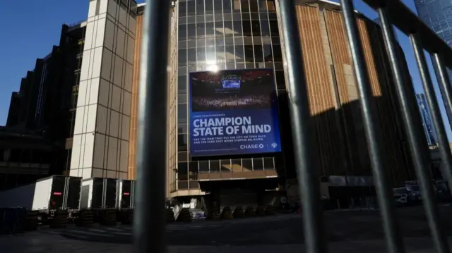 Madison Square Garden as pictured through a fence, rows of lorries parked outside