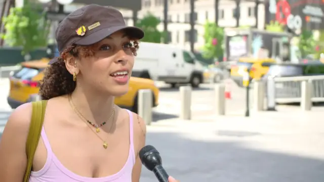 A woman in pink vest and black hat speaks into a microphone