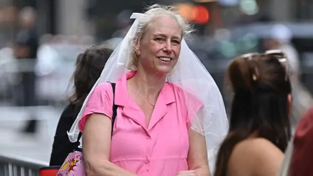 A woman in a pink shirt wears a white wedding veil