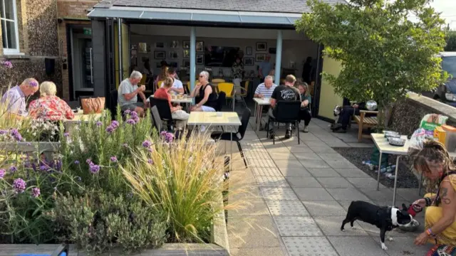 People gathered at tables in the garden of an evacuation centre.