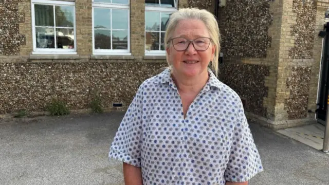 Barbara Buckley Chair of Westleton Village Hal in a patterned white shirt. She has light coloured hair and wears glasses.