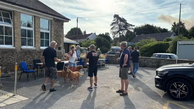 People gather outside a village hall at a long table.
