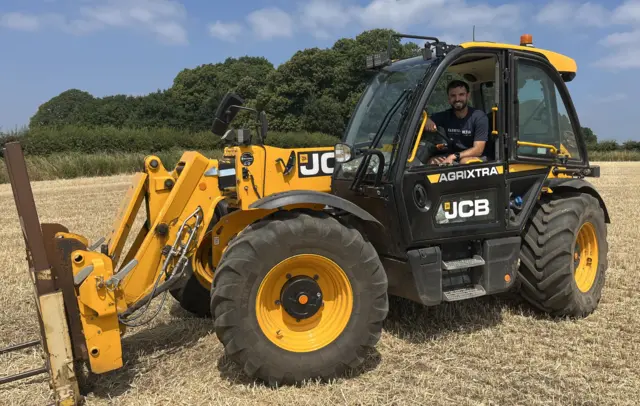 Alex Marshall sits in a large yellow JCB Agrixtra vehicle