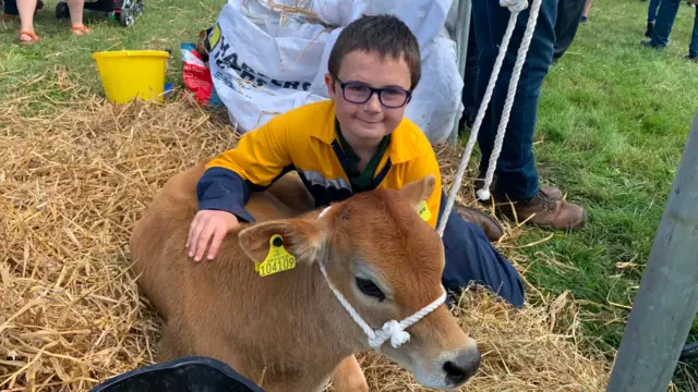A boy wearing a yellow shirt pets a small brown cow