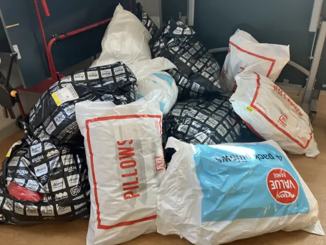 Bags filled with pillows and other items in a pile within a village hall.