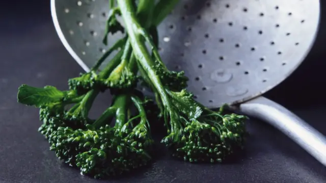 Two green florets of tenderstem broccoli lie on a colander