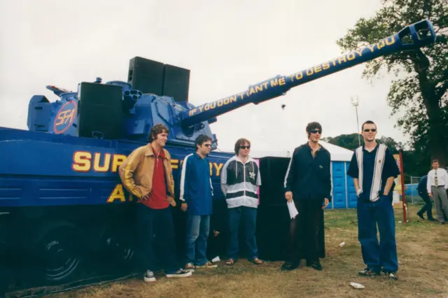 Aelodau'r band o flaen y tanc ar Faes yr Eisteddfod Genedlaethol yn Llandeilo yn 1996