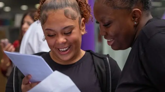 Two teenagers smile as they look at their exam results