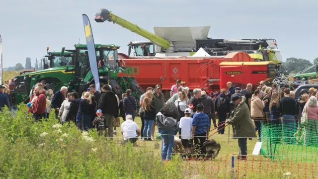 A group of people stand in front of a large combine harvester in a field