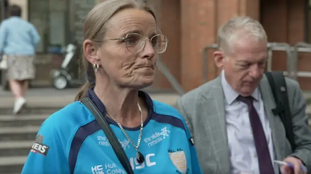 Joanne Moody speaks outside court, wearing a blue top and necklace, with her lips pursed.