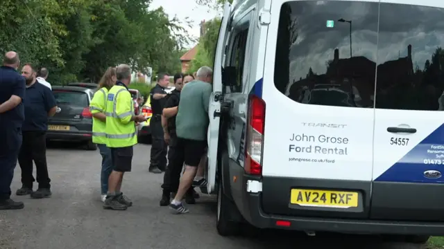 The back view of a white mini van at Westleton. A man is climbing into it. Behind him are two officials in hi-vis jackets.