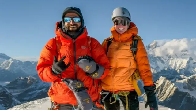 Duas pessoas vestindo casacos laranja sorrindo para a câmera em uma montanha