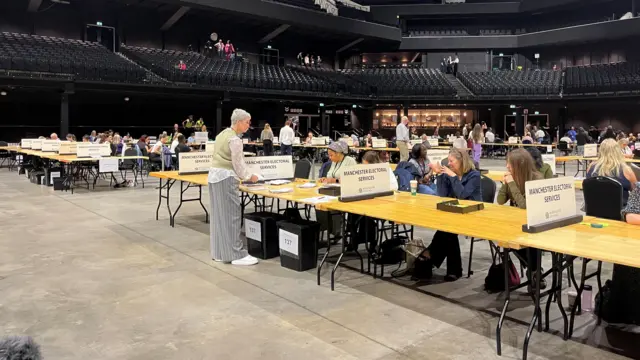 People sitting or standing near counting tables in the arena.