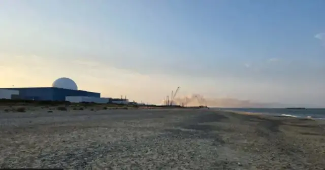 A power plant is on the left and in the distance smoke can be seen