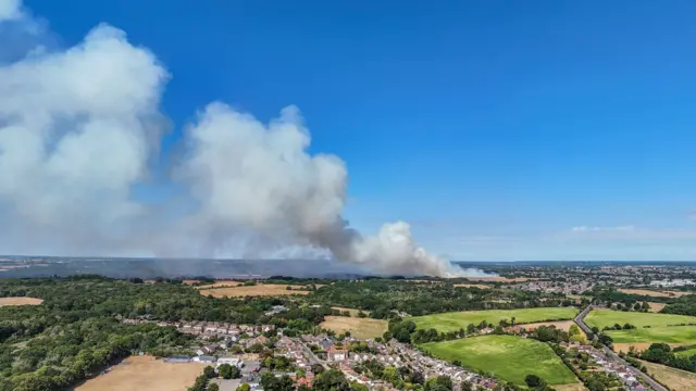 A drone shot of houses, fields and smoke filling the sky.