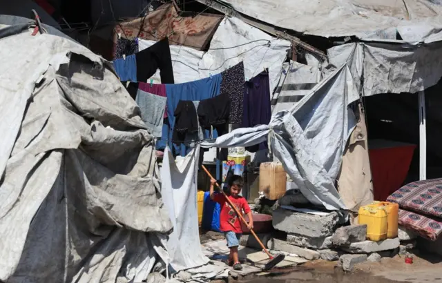 A child walks carrying a broom as displaced Palestinians shelter at a tent camp, in Gaza City, July 31.