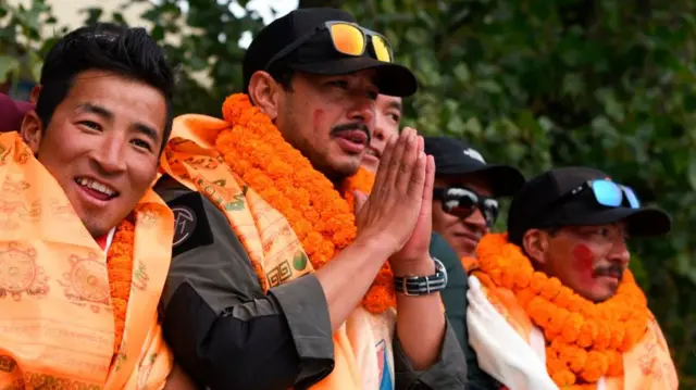 Nirmal Purja with orange garlands of flowers, presses his palms together