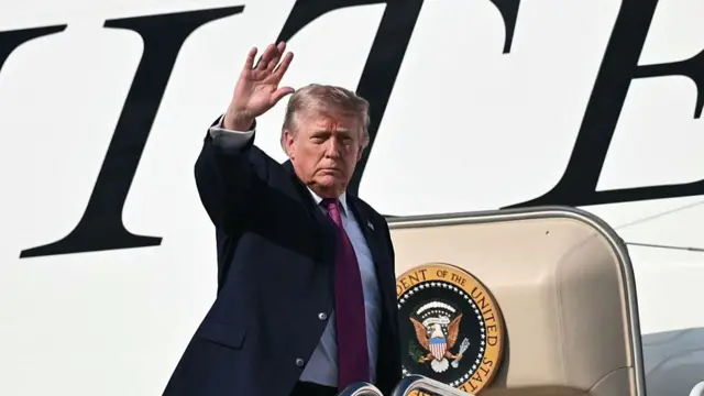 US President Donald Trump in a black suit waves as he boards Air Force One