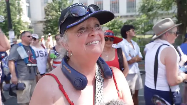 Tammy Wapshott smiling, wears a hat with sunglasses, a pair of navy headphones slung around her neck.