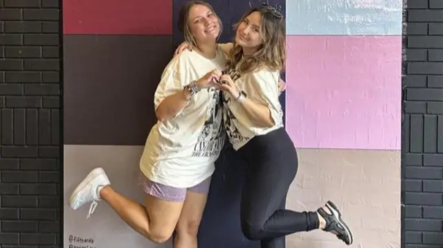 Two women pose in front of a sign painted on a brick wall that says "In My Nashville Era" during Taylor Swift's Eras tour
