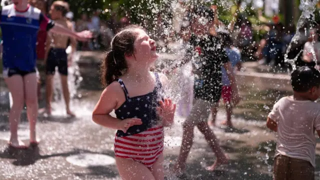 A girl wearing a US themed swimming costume plays in a fountain during the heatwave